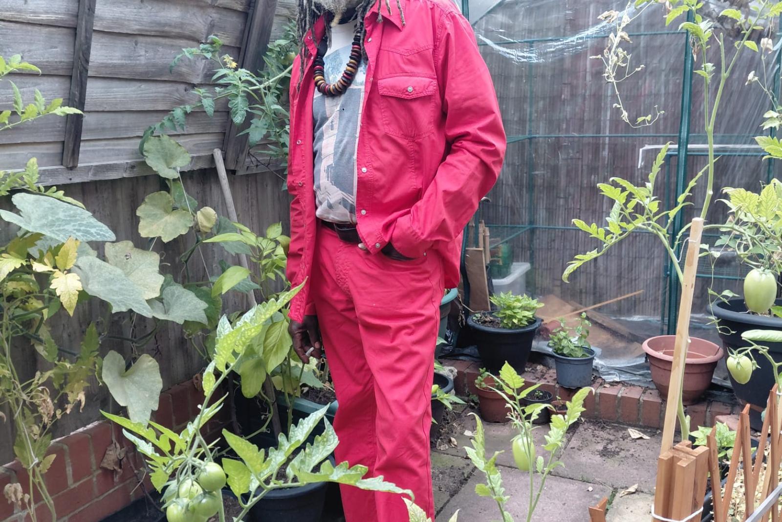 Fyah Mawi in a red suit beside garden plants.