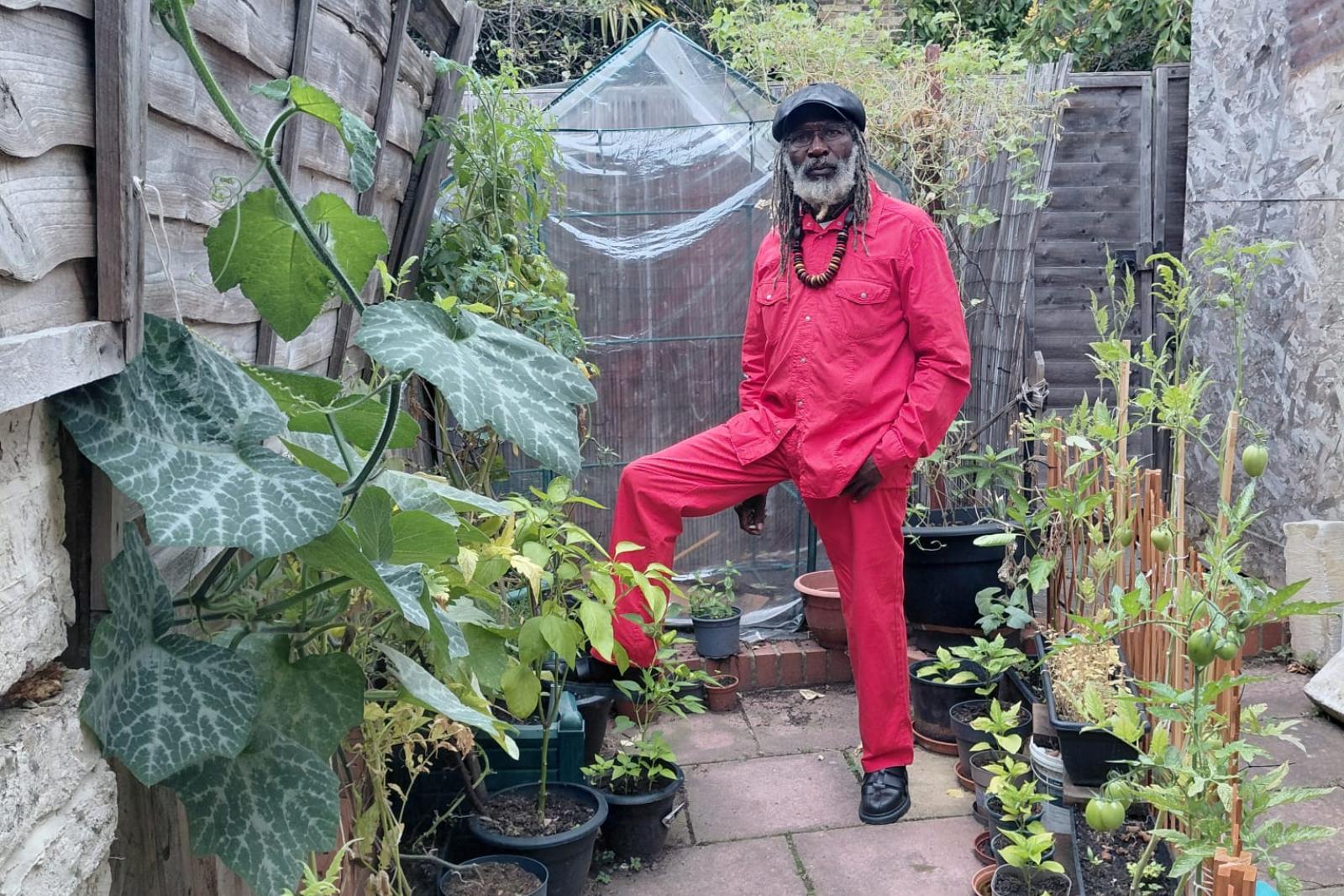 Fyah Mawi seated on a garden bench in a red suit.