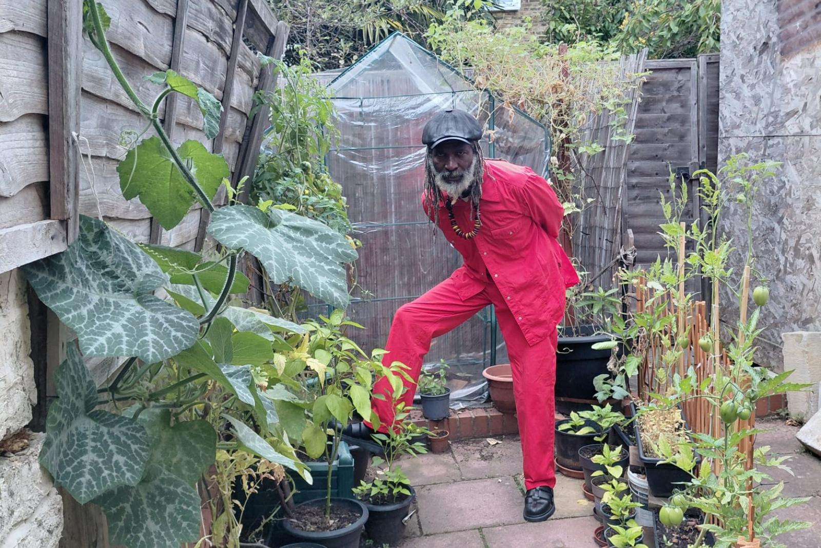 Fyah Mawi seated in a red suit beside a garden path.