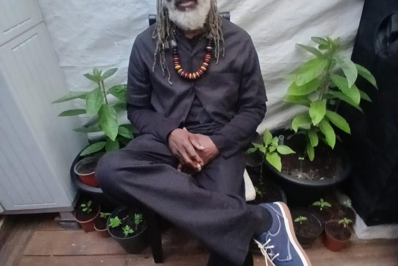 Fyah Mawi seated in a dark suit and cap.