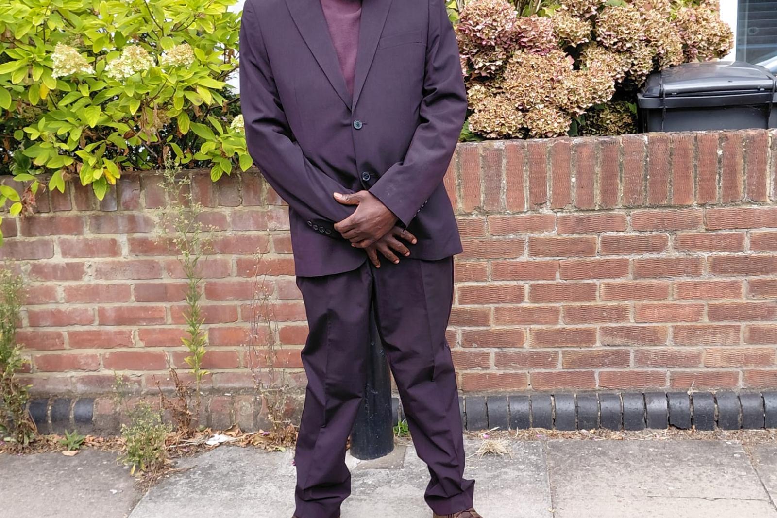 Fyah Mawi standing on the pavement in a dark suit.