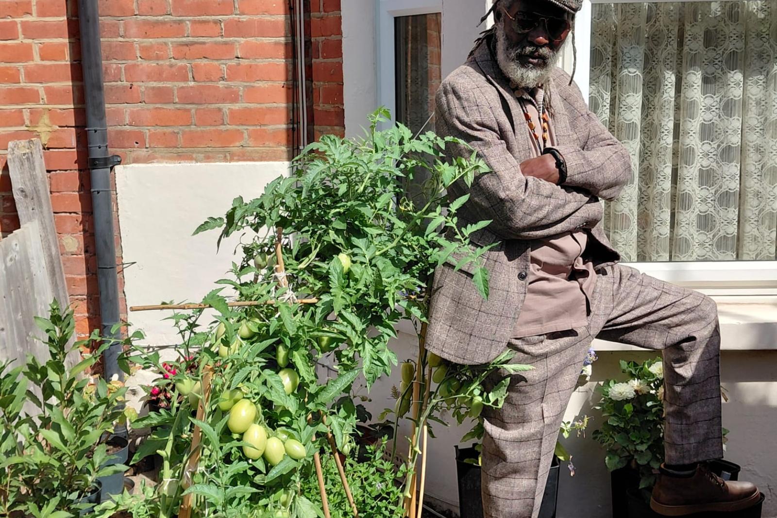 Fyah Mawi in a checked suit beside a garden gate.