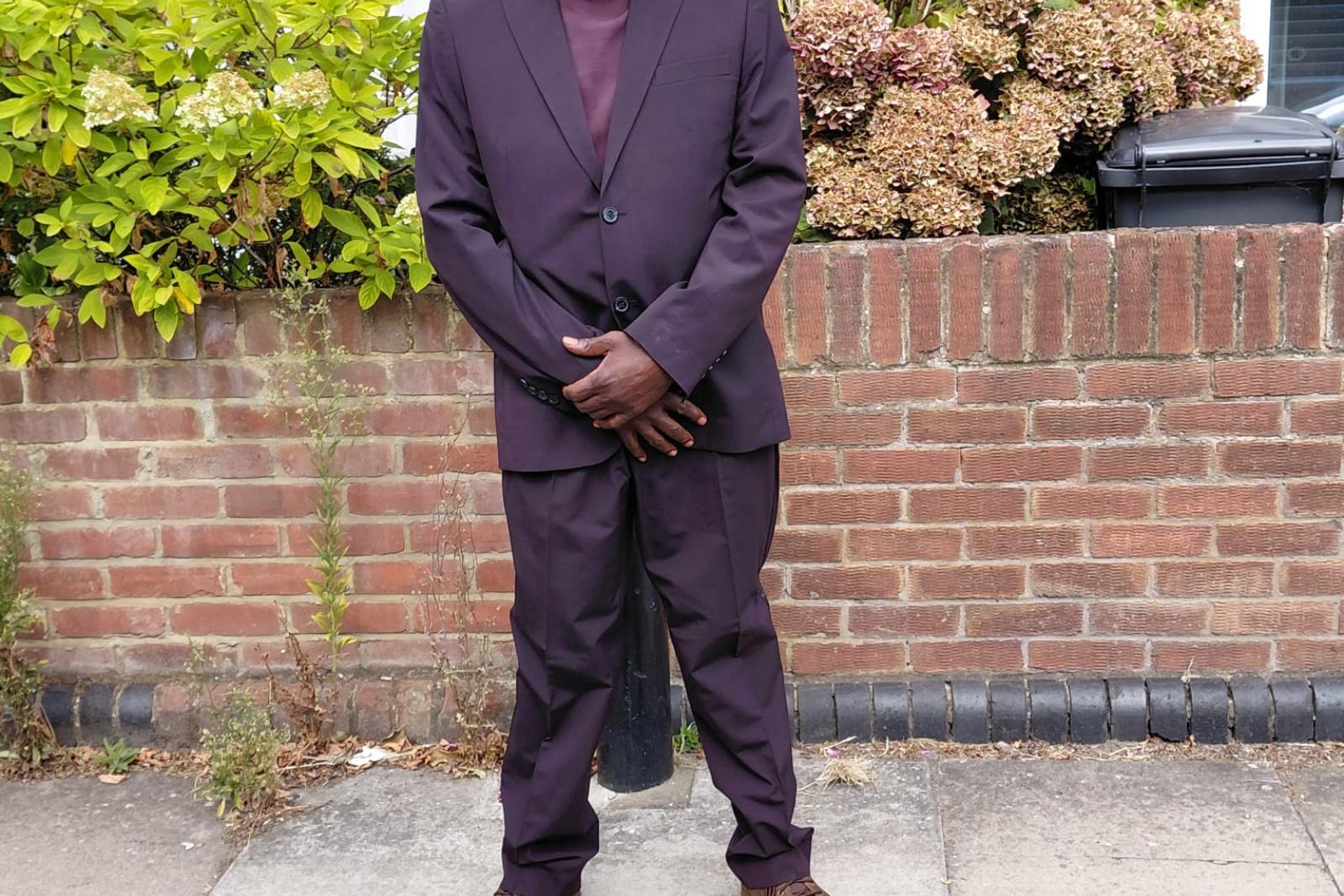 Fyah Mawi in a dark suit outside a brick house.