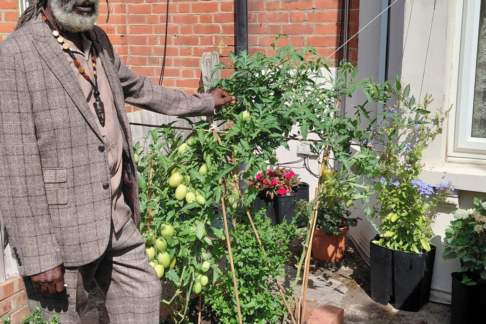 Fyah Mawi wearing a checked suit beside garden plants.