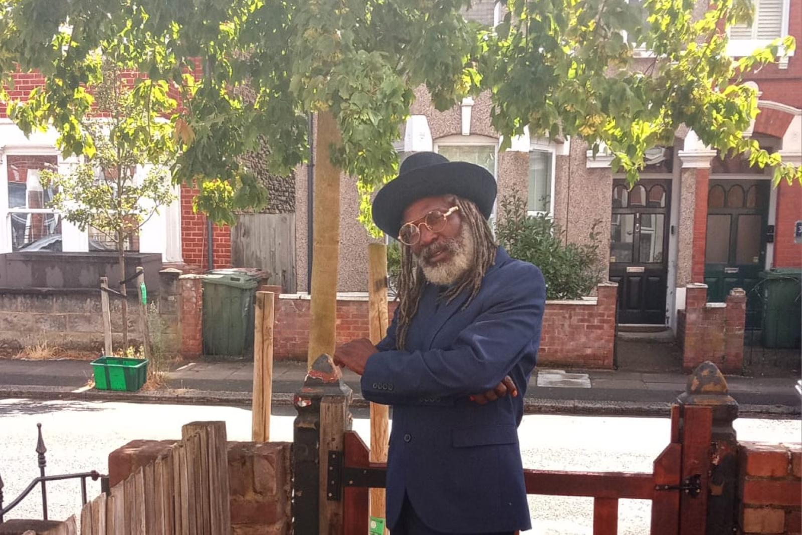 Fyah Mawi in a blue suit beneath garden trees.