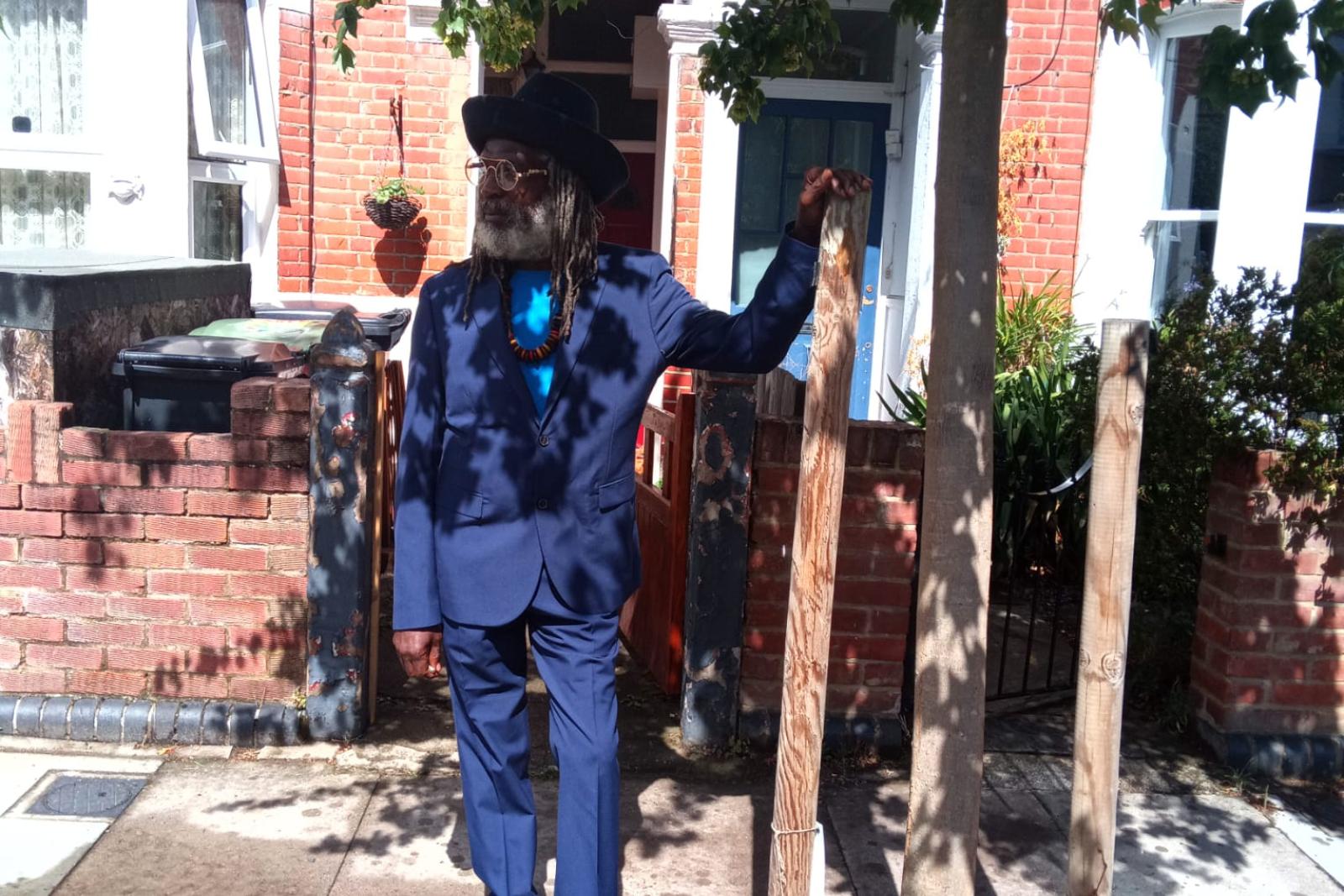 Fyah Mawi standing beneath a tree in a blue suit.