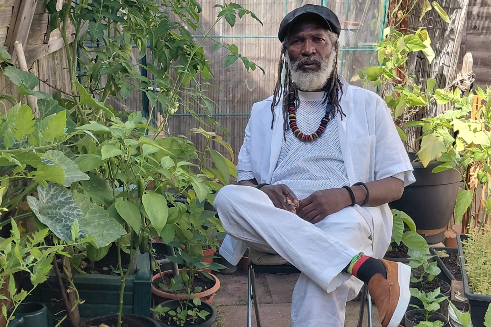 Fyah Mawi in a light suit and cap among garden plants.