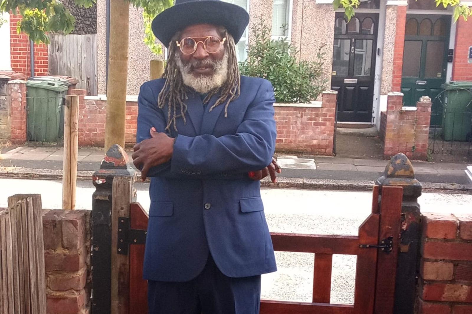 Fyah Mawi standing at a garden gate in a blue suit.