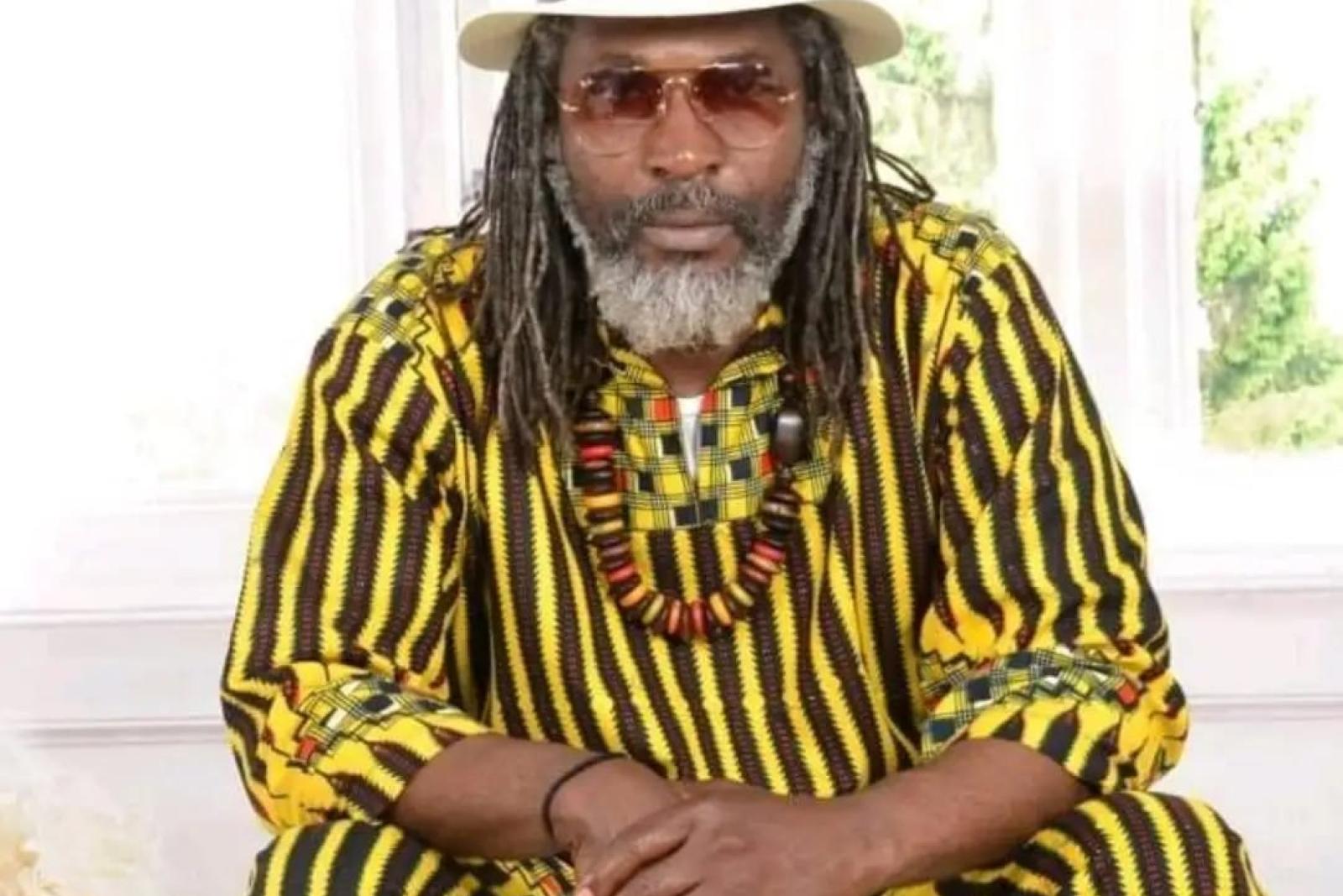 Fyah Mawi seated in a yellow patterned outfit and white hat.