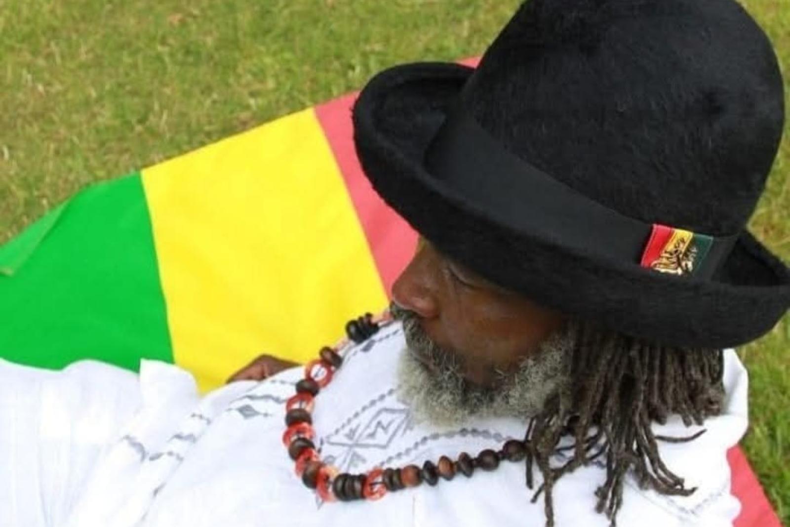 Fyah Mawi wearing a black hat beside red, yellow and green fabric.